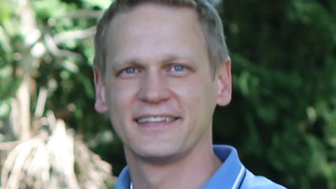 a man wearing a blue shirt and smiling at the camera