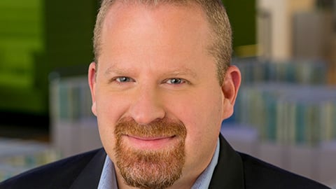 a man wearing a suit and tie smiling and looking at the camera