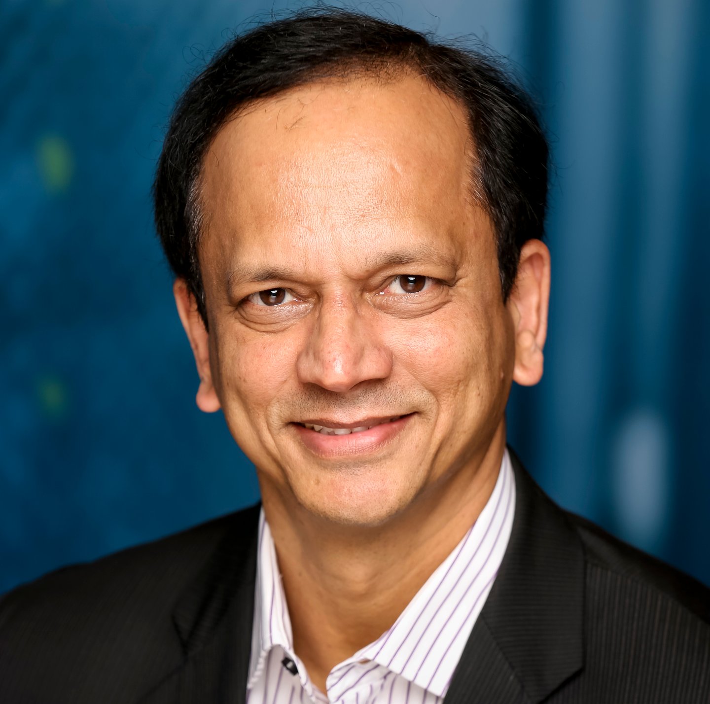 a man wearing a suit and tie smiling and looking at the camera