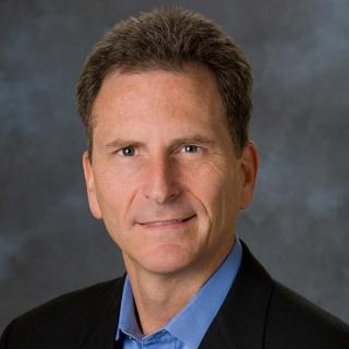 a man wearing a suit and tie smiling and looking at the camera