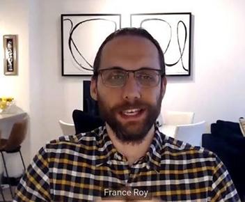 a man sitting at a table with a laptop and smiling at the camera